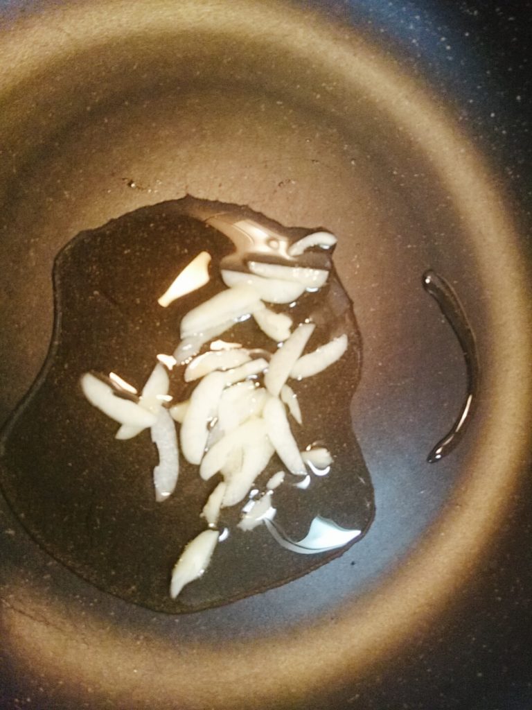 ニンニクのスライスをフライパンで炒めている写真